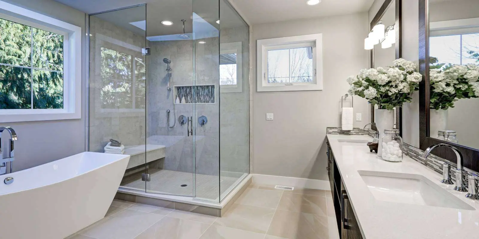 Bright bathroom with a freestanding tub, walk-in glass shower and twin vanities